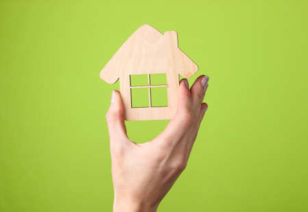 Wooden figurine of house in female hand on green backgroundの写真素材