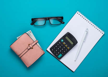 Flat lay economic composition. Calculator, notebook, glasses, wallet on blue background. Family budget. Top viewの写真素材