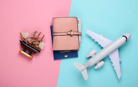 Flat lay travel design. Figurine of a ship, airplane, passport and walet on a blue-pink pastel...