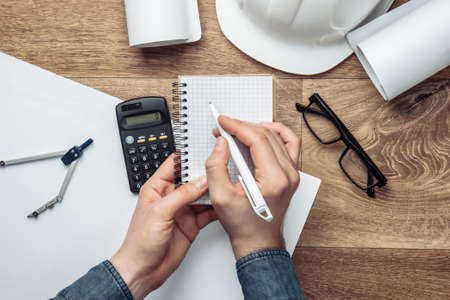 Engineer workspace. Men's hands write in a notebook on the background of the workplace. Top view