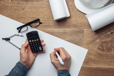 Engineer workspace. Male hands count on the calculator the cost of building a house on a wooden...