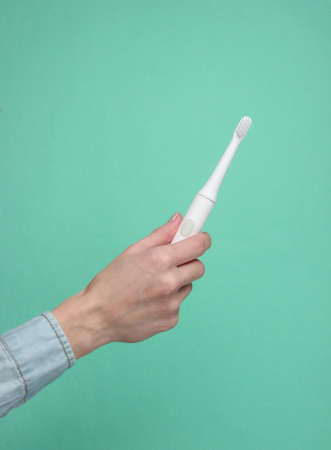 Female hand holds a modern electro toothbrush on a blue backgroundの写真素材