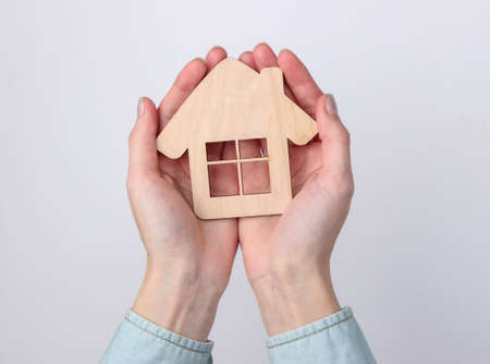 Wooden figurine of a house in female hands on a white backgroundの写真素材