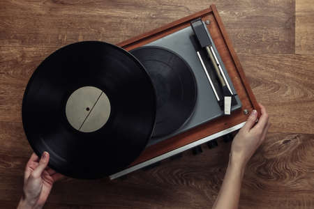 Female hands set up a retro vinyl record player on a wooden floor. Music lover, 70s, nostalgia, top...