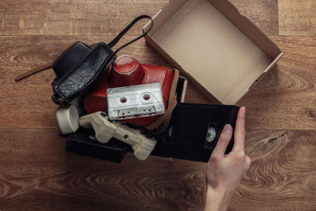 Female hands stack Retro objects in a cardboard box on a wooden floor. Antiques, vintage. Top viewの写真素材