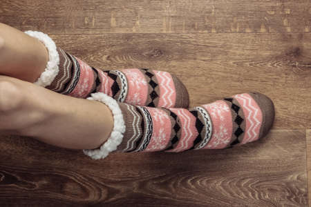 Female legs in warm cozy socks on a wooden floor in the room.