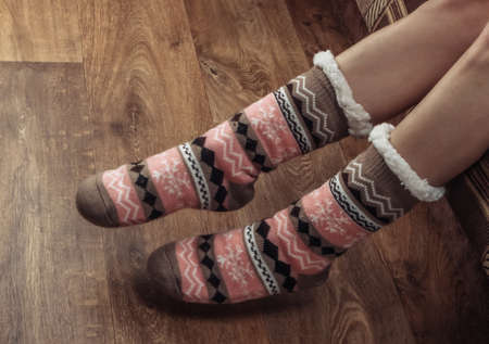 Female legs in warm cozy socks on a wooden floor in the room.