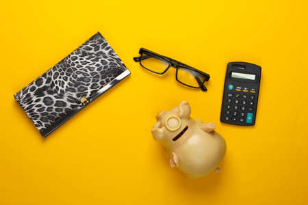 Count Family budget. Piggy bank, wallet, calculator, glasses on yellow background. Flat lay, top...