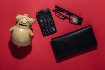 Count Family budget. Piggy bank, wallet, calculator, glasses on a red background. Flat lay, top viewの写真素材