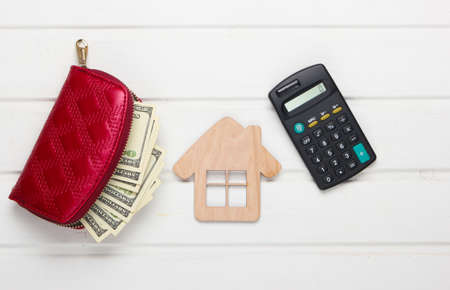 Calculation of rent payment for housing. Creative flat lay composition. House figurine, calculator, wallet with money on a white table. Top viewの写真素材