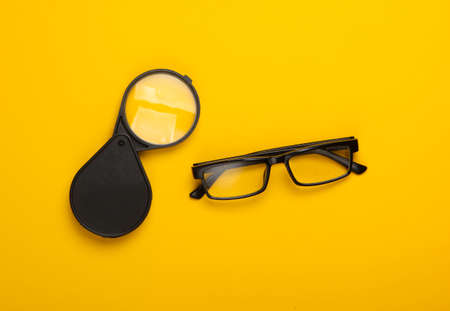 Magnifying glass and glasses on yellow background. Top viewの写真素材