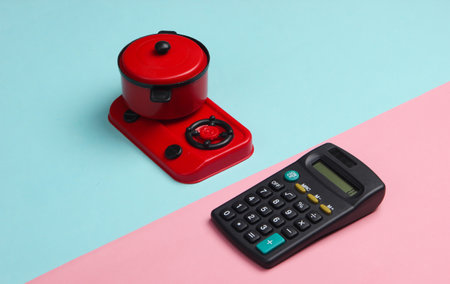 Calculator and toy stove with pan on a blue-pink pastel background. Costing.の写真素材