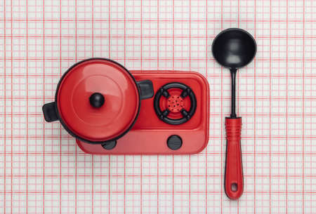 Toy plastic stove with pan, ladle on tablecloth. Kid's Kitchen. Top view, minimalismの写真素材