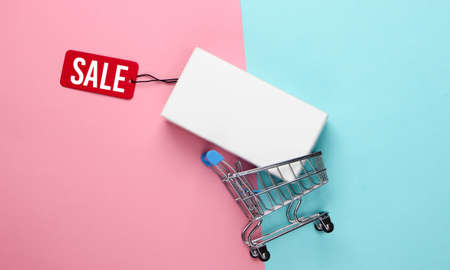 Shopping trolley and white box with tag sale on blue pink background. Minimalism. Top viewの写真素材