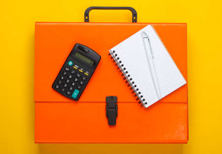 Orange paper case, notebook and calculator on a yellow background. Top viewの写真素材