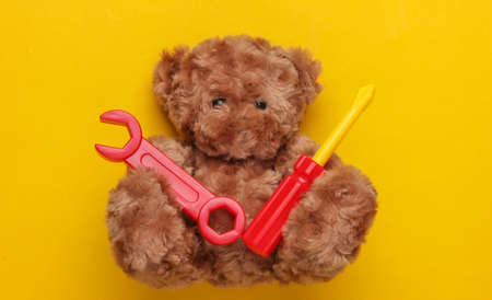 Teddy bear and toy wrench and screwdriver on yellow background. Repair concept. Top view