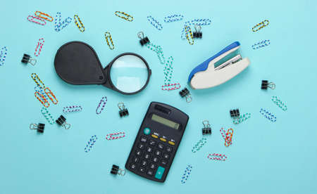 Office tools, stationery. Stapler, calculator, magnifier, paper clips on a blue pastel background. Top viewの写真素材