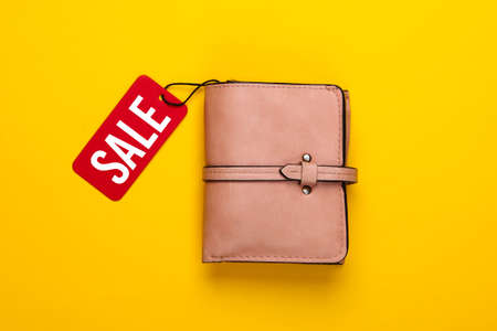 Fashionable leather wallet with red sale tag on yellow background. Top view. Discount. Shopping....