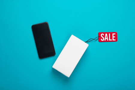 New smartphone and box with tag sale on blue background. Top viewの写真素材