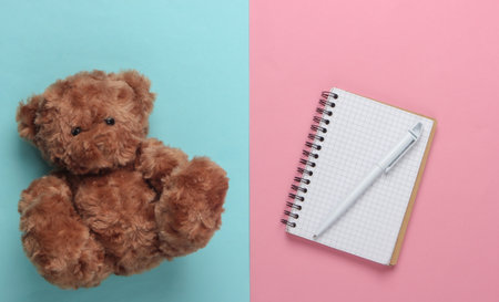 flat lay composition of a teddy bear, notebook with pen on a blue-pink pastel background. Top viewの写真素材