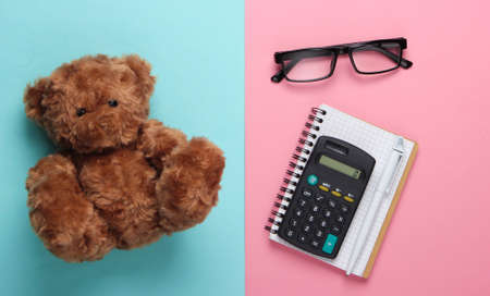 flat lay composition of a teddy bear, notebook with pen, calculator, glasses on a blue-pink pastel background. Top viewの写真素材