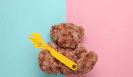 Teddy bear holds toy wrench on a blue pink pastel background. Repair concept. Top viewの写真素材