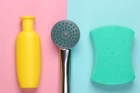 Flat lay composition of shower head for the bathroom and bath products (sponge, shampoo) on blue pink pastel background. Top viewの写真素材