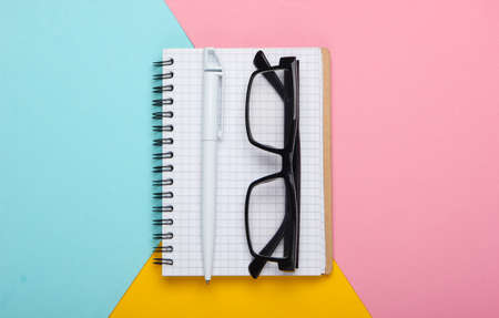 Notebook with glasses on  colored background. Top view, minimalism
