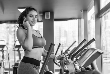 Young attractive woman warming up on an elliptical exercise machine in the gym. Fitness, healthy lifestyle concept.の写真素材