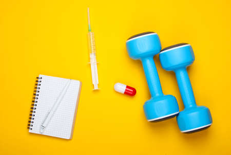 Pharmacology in sports. Dumbbell, capsule, syringe, notebook on yellow background. Vitamins, steroids. Top viewの写真素材