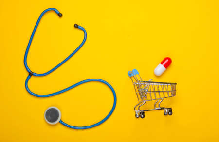 The concept of healing. Flat lay composition. Stethoscope, shopping trolley with capsule on a yellow background. Top viewの写真素材