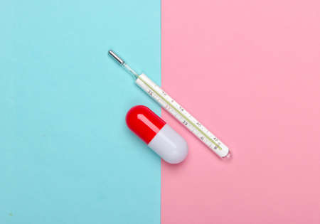 Pill capsule and thermometer on a blue pink pastel background. Top view. Minimalism