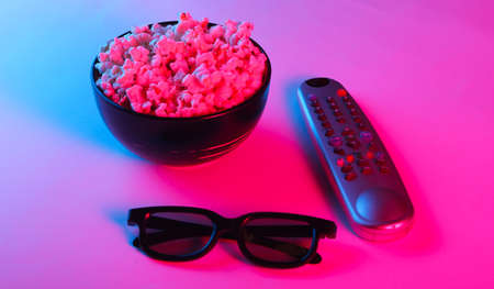 Tv remote, 3d glasses and a bowl of popcorn. Neon pink blue light. Leisure and entertainment concept. Top viewの写真素材