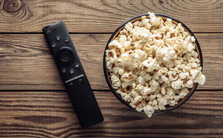 Bowl of popcorn, tv remote on wodden table. Leisure and entertainment concept. Top viewの写真素材