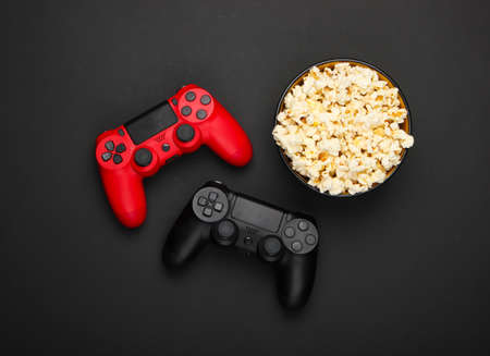 Two gamepads and a bowl of popcorn on black background. Gaming, leisure and entertainment concept....