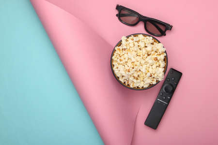 Bowl of popcorn, 3d glasses, tv remote on blue pink background. Leisure and entertainment concept....
