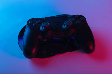 Gamepad and cd compact discs with pink blue neon light. Gaming, entertainment concept.の写真素材