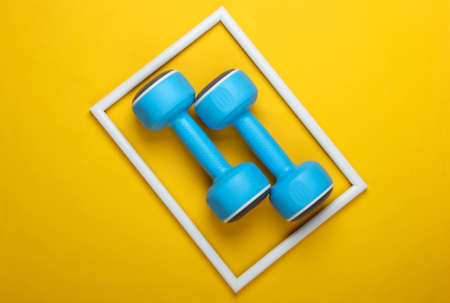 Plastic dumbbell on yellow background with white frame. Fashion shot. Creative flat lay. Top view. Minimalismの写真素材
