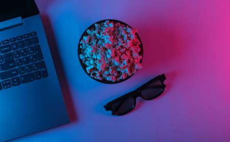 Laptop and bowl of popcorn, 3d glasses with blue pink neon light. Leisure and entertainment concept. Top viewの写真素材