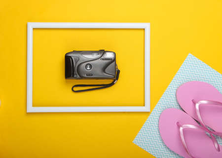Flip flops and retro camera on yellow background with white frame. Studio shot. Creative beach...