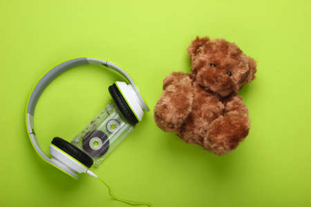 Teddy bear and stereo headphones with audio cassette on a green background. Music lover concept,...