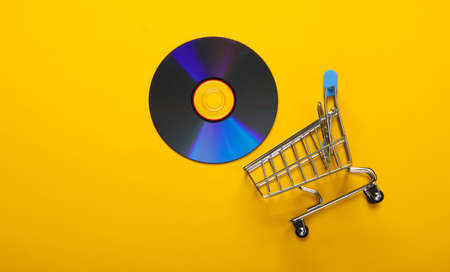 Shopping trolley with cd disk on yellow background. Top view