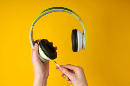 Hand holds and connects a cable to stereo headphones on a yellow background.の写真素材