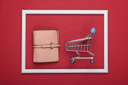 Shopping trolley with leather wallet in a white frame on red background. Shopping concept. Top viewの写真素材