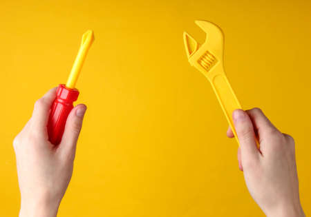 Hands holding a toy screwdriver and wrench on a yellow background.の写真素材