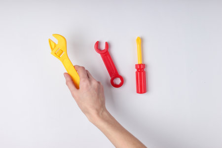 Hands holding a toy screwdriver and wrench on white background. Top view
