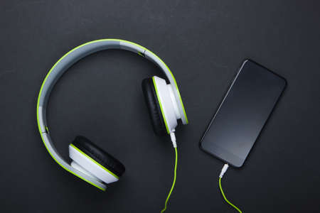 Stylish wired stereo headphones with smartphone on black background. Music lover. Modern gadgets. Top view. Minimalismの写真素材