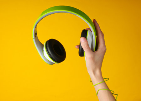 Hand wrapped in cable holds stereo headphones on a yellow backgroundの写真素材