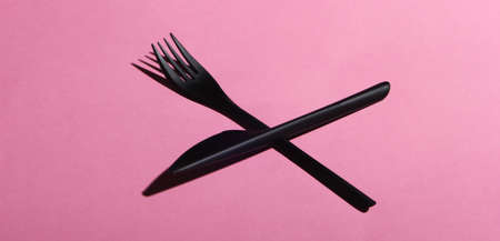 Black plastic knife and fork on pink pastel background. Food minimalism
