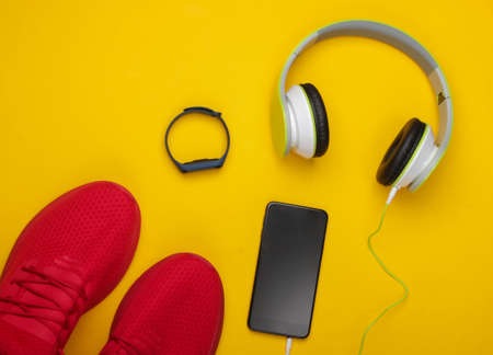 Flat lay composition of modern gadgets for sports and fitness. Headphones, smart bracelet, smartphone, running shoes on yellow background. Top viewの写真素材